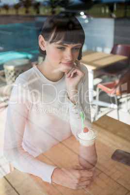 Woman sitting in cafeteria with milkshake on table