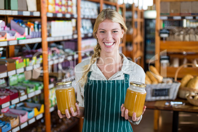 Smiling female staff holding jars of honey in supermarket