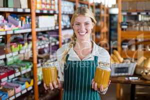 Smiling female staff holding jars of honey in supermarket