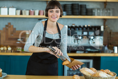 Smiling waitress packing croissants in paper bag at cafÃ?Â©