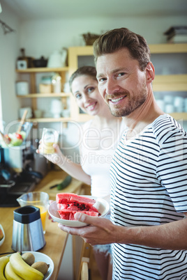 Smiling couple holding plate of water melon in kitchen