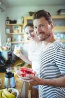 Smiling couple holding plate of water melon in kitchen