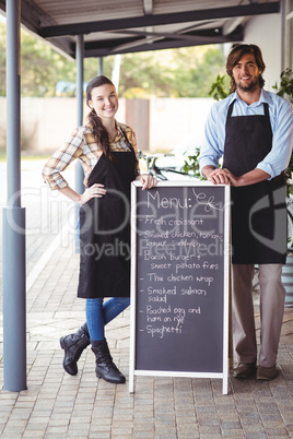 Waiter and waitress standing with menu board outside the cafe