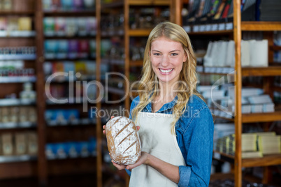 Smiling female staff holding bread in supermarket