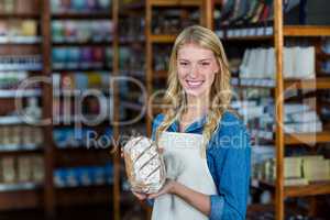 Smiling female staff holding bread in supermarket