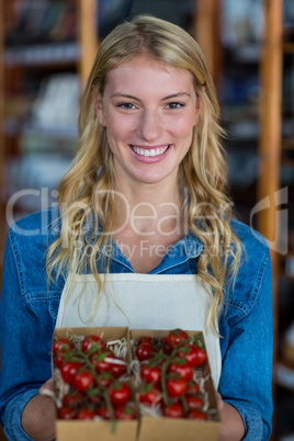 Smiling female staff holding box of cherry tomato in supermarket