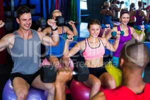 Smiling friends holding dumbbells while sitting on exercise ball