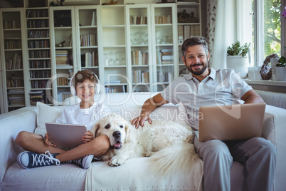 Father and son sitting on sofa and using digital tablet and laptop