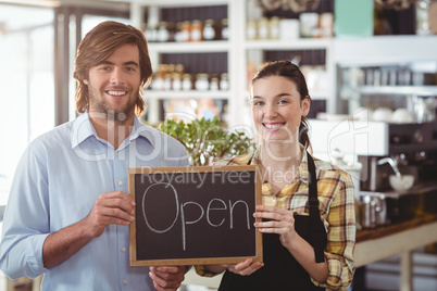 Portrait of man and waitress holding chalkboard with open sign