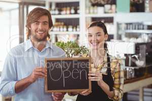 Portrait of man and waitress holding chalkboard with open sign