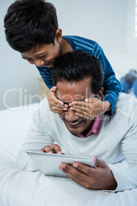 Son covering fathers eyes from behind on the bed