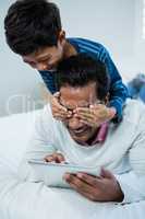 Son covering fathers eyes from behind on the bed