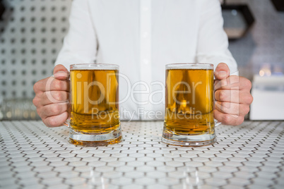 Bartender holding two glass of beer in bar counter