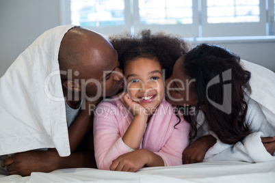Father and mother kissing their daughter on bed