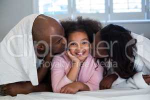 Father and mother kissing their daughter on bed