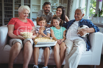 Multi-generation family sitting with popcorn and pizza while watching soccer match