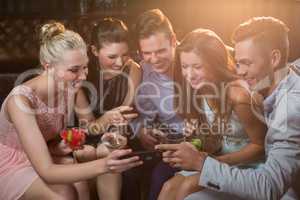 Smiling friends looking at mobile phone while having cocktail