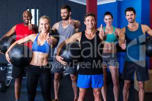 Portrait of happy friends showing thumbs up in gym