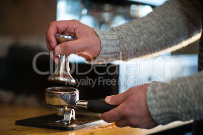 Waiter using a tamper to press ground coffee into a portafilter