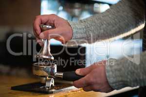 Waiter using a tamper to press ground coffee into a portafilter