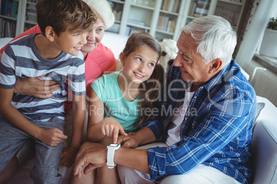 Grandparents and grandchildren looking at smartwatch in living room