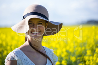 Portrait of happy woman wearing hat and standing in mustard field