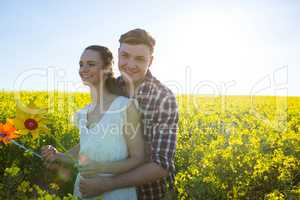Couple holding pinwheel and embracing each other in mustard field