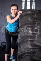 Portrait of confident female athlete pushing tire in gym