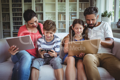 Happy family sitting on sofa and using laptop, mobile phone and digital tablet