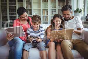 Happy family sitting on sofa and using laptop, mobile phone and digital tablet