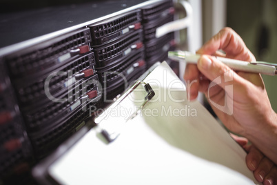 Close-up of technician maintaining record of rack mounted server on clipboard