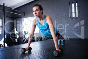Sporty young woman doing push-ups with dumbbells