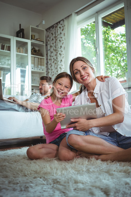 Mother and daughter sitting on floor and using digital tablet