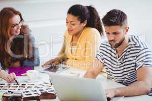 Editor using laptop with colleagues talking at creative office