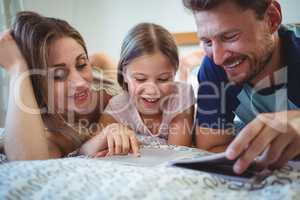 Parents lying with daughter on bed and looking at photo album