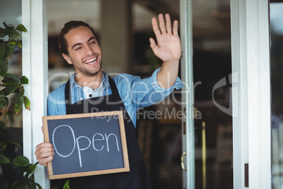 Waiter standing at cafe door holding chalkboard with open sign