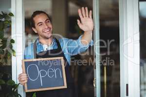 Waiter standing at cafe door holding chalkboard with open sign