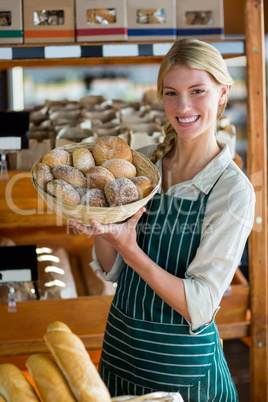 Smiling female staff holding basket of sesame breads at bread counter