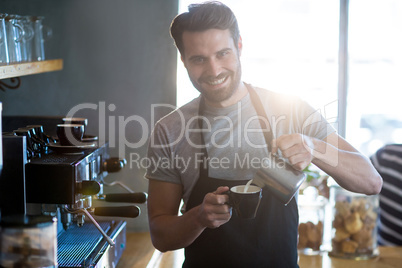 Smiling waiter making cup of coffee at counter in cafe