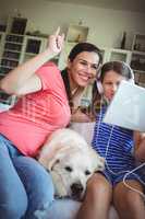 Happy mother and daughter sitting with pet dog and using digital