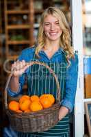 Smiling female staff holding basket of fruit in organic section of supermarket