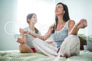 Mother and daughter performing yoga on bed