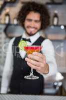 Bartender holding glass of cocktail in bar counter