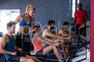 People using rowing machine with fitness instructor in gym