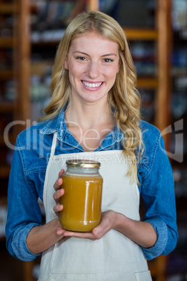 Smiling female staff holding jar of honey in supermarket