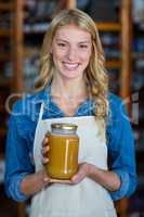 Smiling female staff holding jar of honey in supermarket