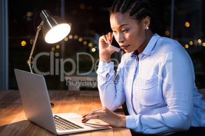 Businesswoman talking on mobile phone while working on laptop