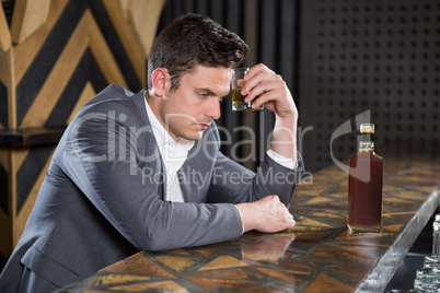 Depressed man having glass of whisky at counter