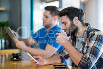 Men using mobile phone and digital tablet while having cup of coffee