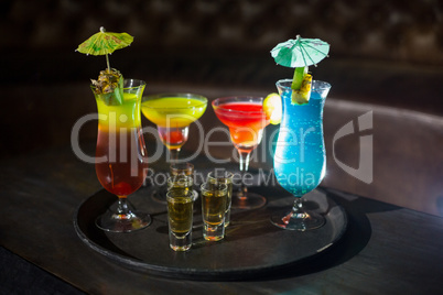 Various cocktail drinks and shot glasses of tequila on serving tray